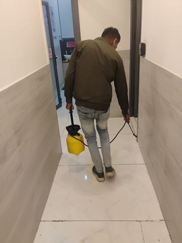 Technician walking a corridor with a pressure sprayer during a scheduled treatment