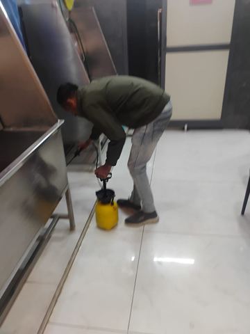 Technician treating beneath stainless steel equipment in a commercial premises